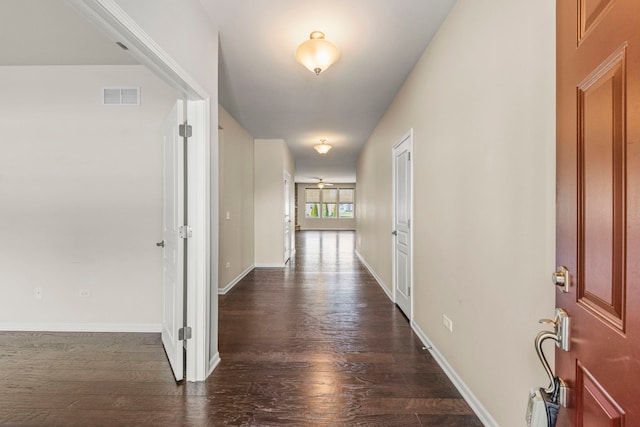 corridor with dark wood-style flooring, baseboards, and visible vents