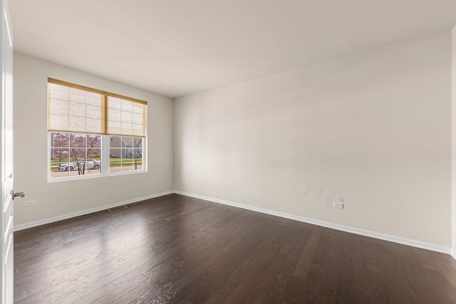 spare room with dark wood-type flooring, visible vents, and baseboards
