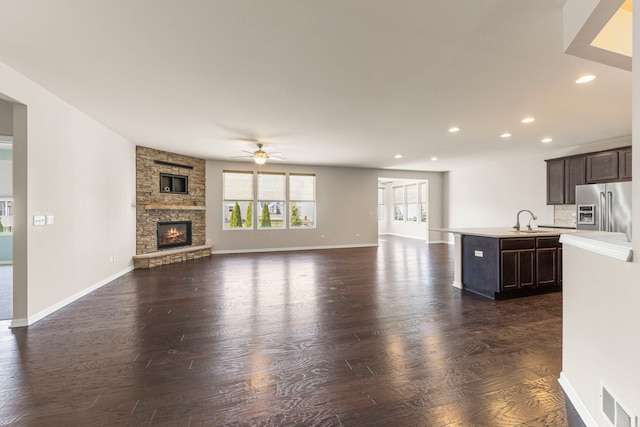 unfurnished living room with visible vents, a sink, dark wood-style flooring, ceiling fan, and a stone fireplace