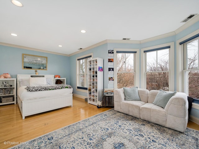bedroom with wood finished floors, baseboards, ornamental molding, and visible vents