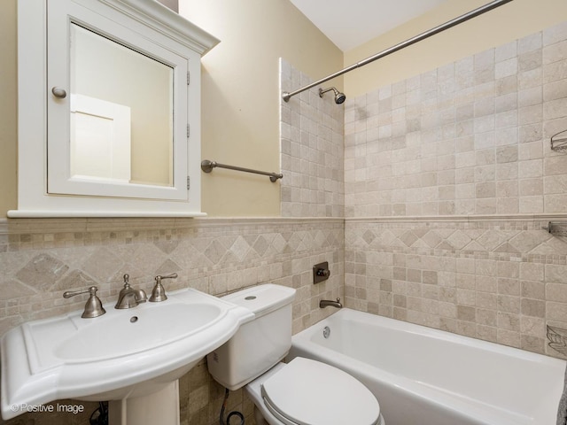 bathroom with a sink, toilet, tile walls,  shower combination, and wainscoting