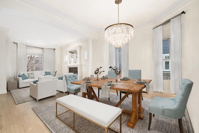 dining room with a chandelier, a fireplace, crown molding, ornate columns, and hardwood / wood-style flooring