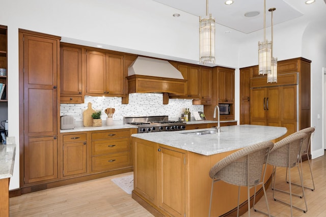 kitchen with custom exhaust hood, brown cabinetry, light wood-type flooring, and a sink