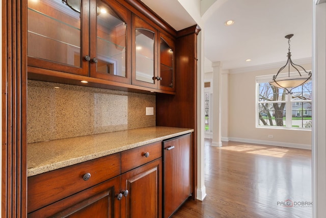 kitchen featuring light stone counters, decorative backsplash, glass insert cabinets, baseboards, and brown cabinetry