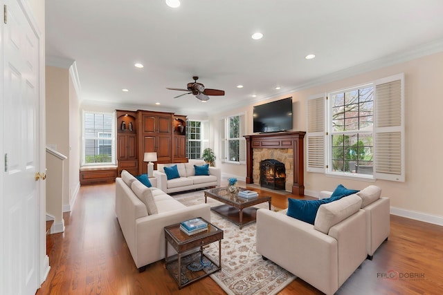 living room with crown molding, a stone fireplace, ceiling fan, and baseboards