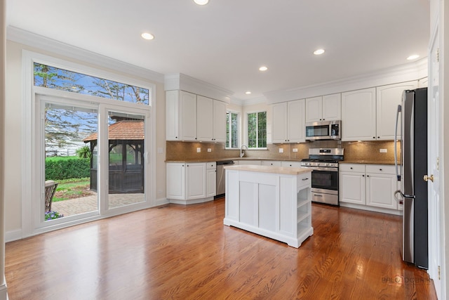 kitchen featuring stainless steel appliances, decorative backsplash, ornamental molding, white cabinets, and wood finished floors