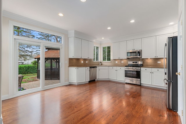 kitchen with crown molding, appliances with stainless steel finishes, white cabinets, backsplash, and dark wood-type flooring