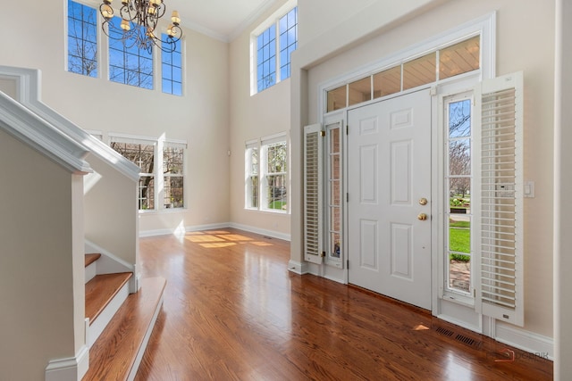 foyer entrance with ornamental molding, an inviting chandelier, wood finished floors, and plenty of natural light