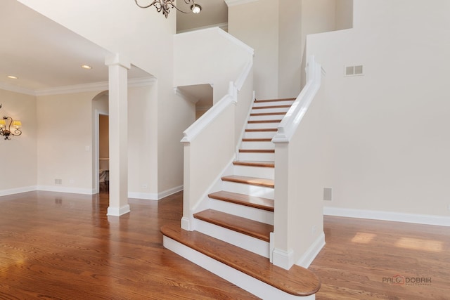 stairs with a chandelier, arched walkways, wood finished floors, and crown molding