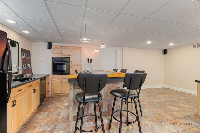 kitchen with a kitchen breakfast bar, a sink, light brown cabinets, black appliances, and a paneled ceiling