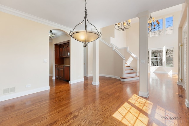 unfurnished dining area with an inviting chandelier, stairway, visible vents, baseboards, and wood finished floors