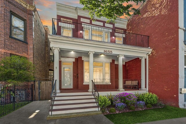 1655 W Byron St, Chicago, IL 60613 - exterior entry at dusk featuring brick siding, a balcony, a porch, and fence