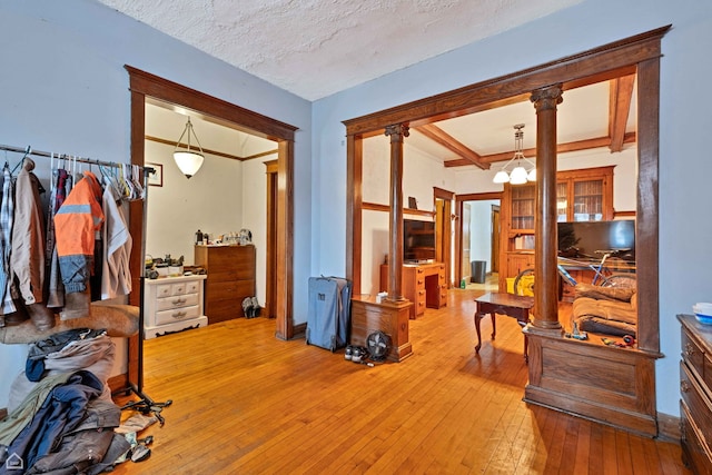bedroom with beam ceiling, a textured ceiling, decorative columns, and light wood finished floors