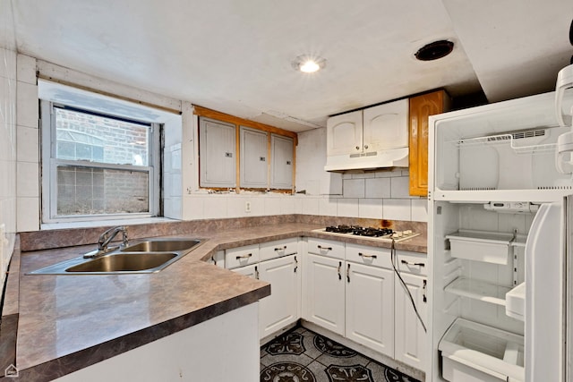 kitchen with dark tile patterned floors, white cabinetry, under cabinet range hood, white gas stovetop, and a sink