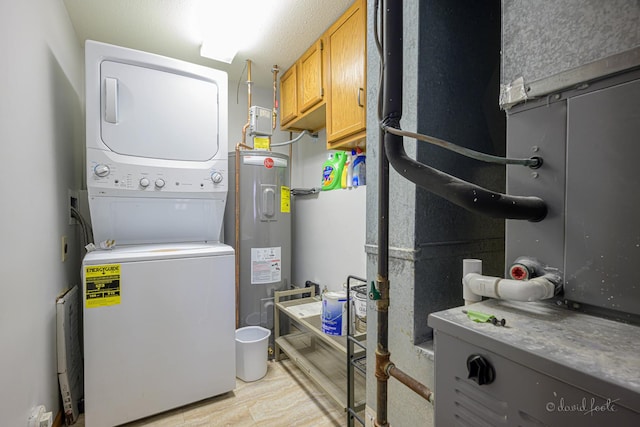 clothes washing area with cabinet space, stacked washing maching and dryer, and water heater