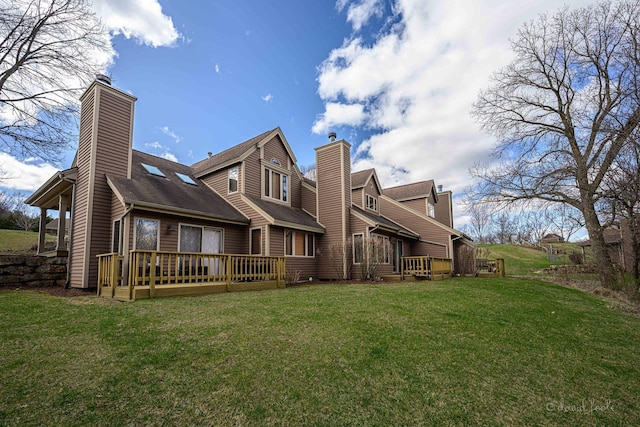 back of property with a wooden deck, a shingled roof, a lawn, and a chimney