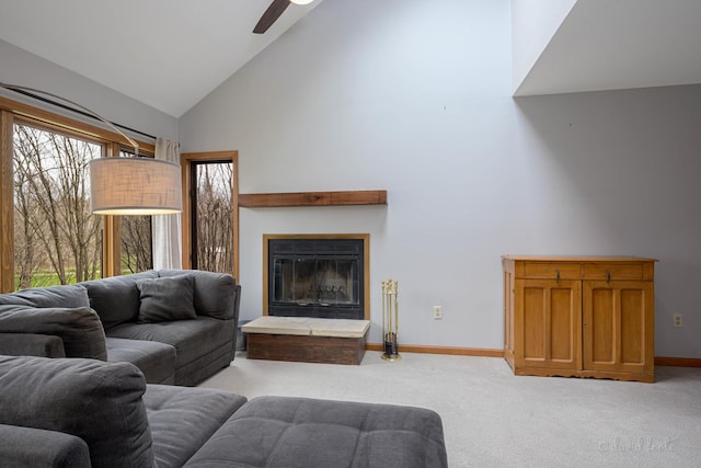 living room with ceiling fan, high vaulted ceiling, a glass covered fireplace, light carpet, and baseboards