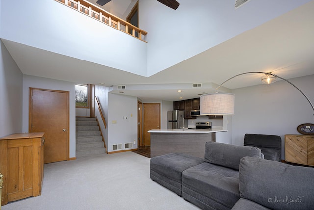 living room featuring visible vents, ceiling fan, stairway, and light colored carpet