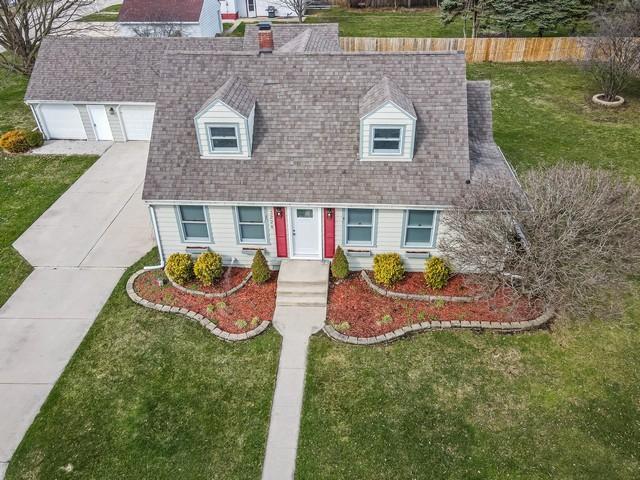 new england style home featuring roof with shingles, a garage, a front yard, and driveway