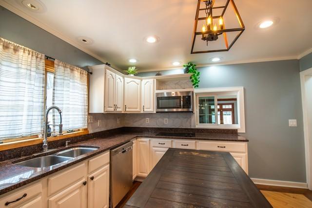 kitchen featuring crown molding, recessed lighting, dark stone countertops, appliances with stainless steel finishes, and a sink
