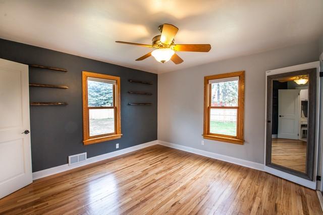 unfurnished bedroom with wood finished floors, baseboards, multiple windows, and visible vents