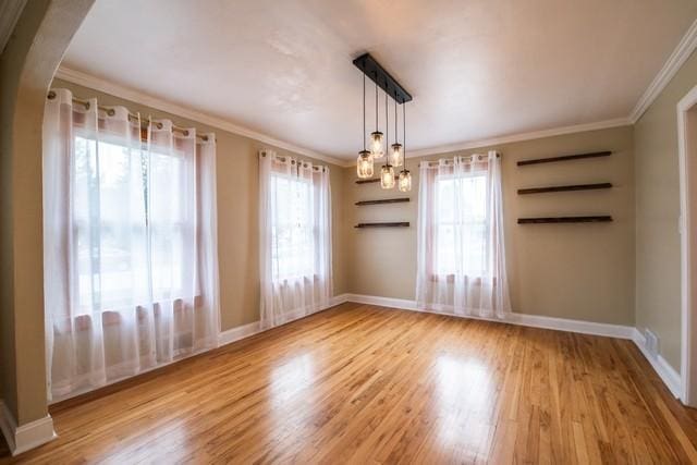 spare room with arched walkways, baseboards, ornamental molding, and wood finished floors