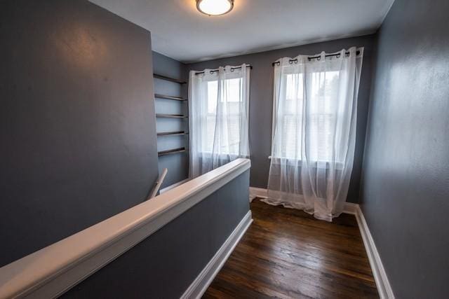 corridor featuring baseboards and dark wood finished floors