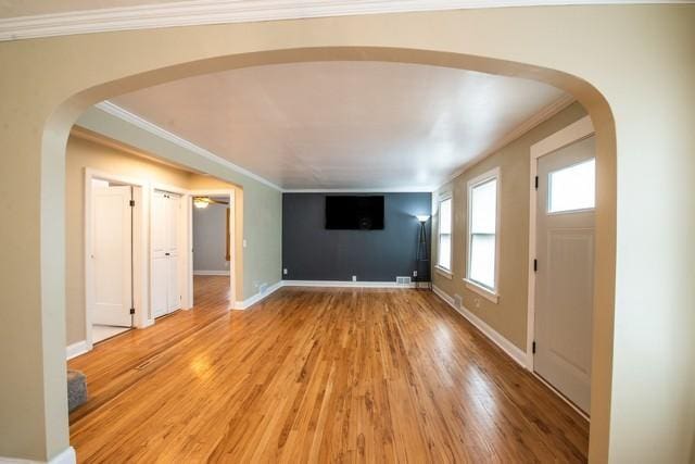 unfurnished living room with baseboards, arched walkways, light wood-type flooring, and crown molding