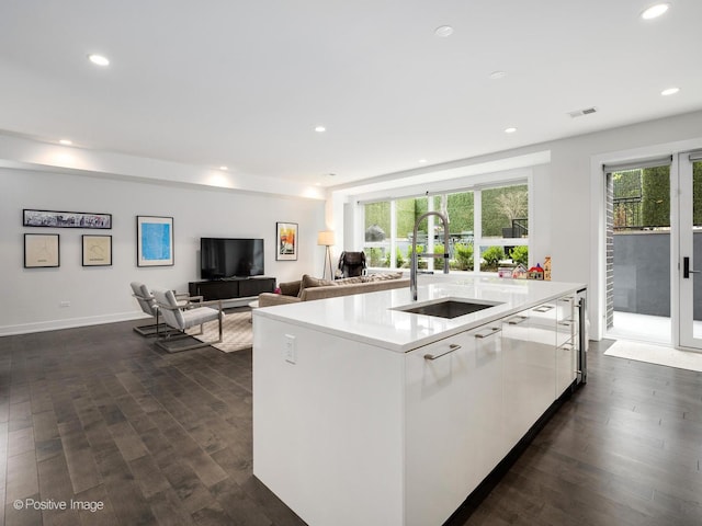 kitchen with dark wood finished floors, white cabinetry, visible vents, a kitchen island with sink, and a sink