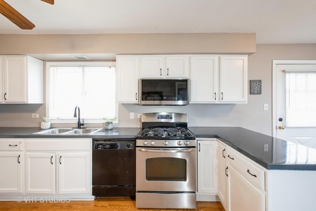 kitchen with a peninsula, dark countertops, white cabinets, stainless steel appliances, and a sink