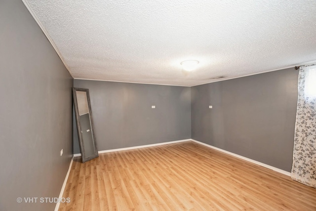 unfurnished room featuring ornamental molding, baseboards, light wood finished floors, and a textured ceiling