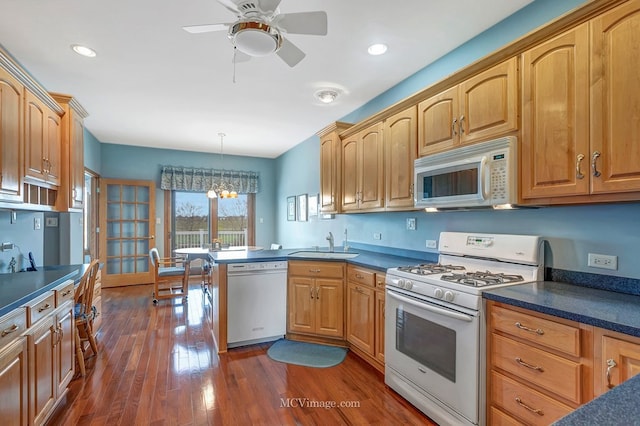 kitchen featuring white appliances, dark wood-style floors, a sink, and dark countertops