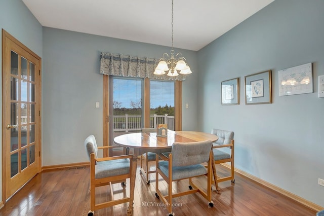 dining area featuring wood-type flooring, a notable chandelier, baseboards, and visible vents