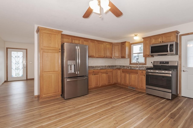 kitchen featuring stainless steel appliances, a sink, light wood-style floors, and tasteful backsplash