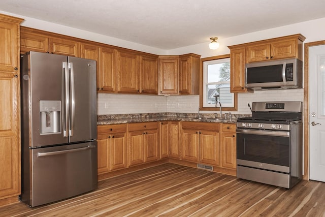 kitchen featuring brown cabinets, appliances with stainless steel finishes, tasteful backsplash, and a sink
