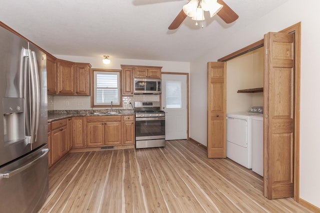 kitchen featuring light wood finished floors, a sink, washer and dryer, and appliances with stainless steel finishes
