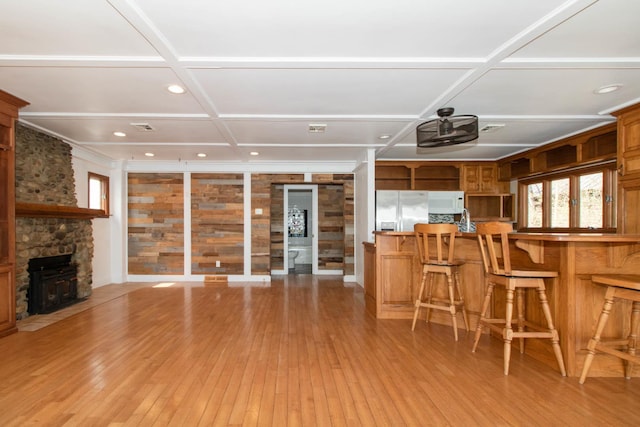 kitchen with coffered ceiling, white microwave, a kitchen bar, brown cabinetry, and stainless steel refrigerator with ice dispenser