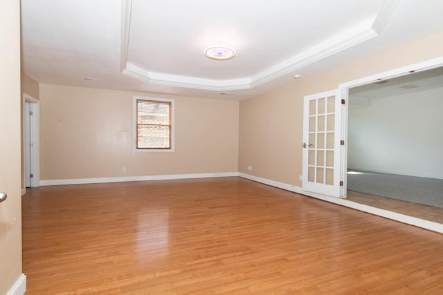 spare room with light wood-style flooring, baseboards, and a raised ceiling