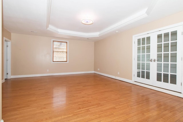 empty room featuring light wood-type flooring, french doors, baseboards, and a raised ceiling