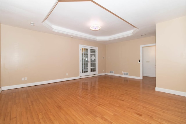 unfurnished room with a tray ceiling, light wood-type flooring, visible vents, and baseboards