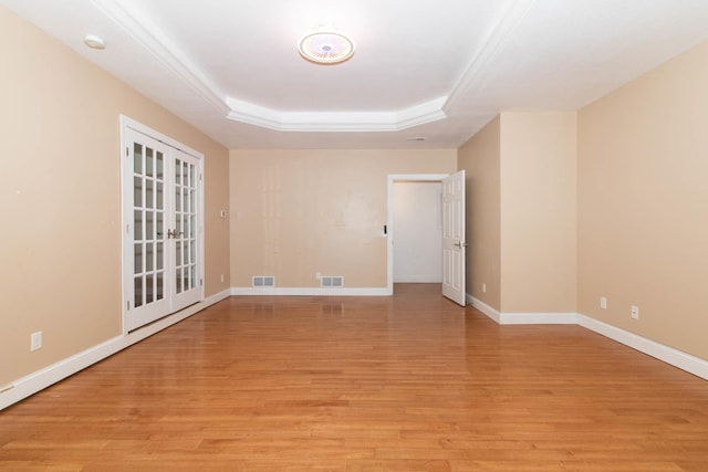 spare room with visible vents, baseboards, a tray ceiling, and light wood finished floors