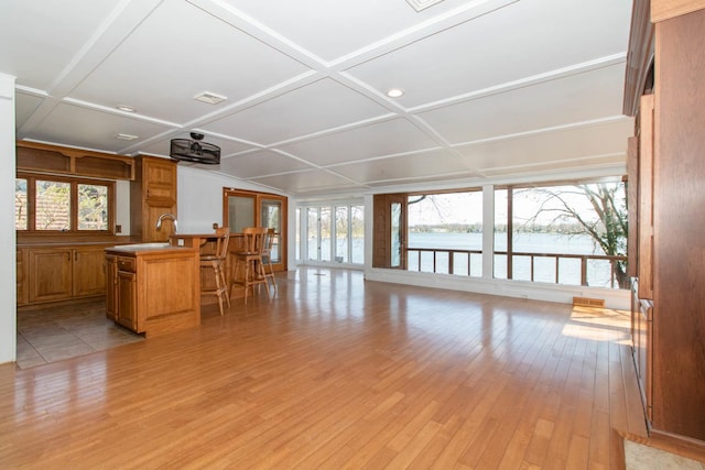 living area with a water view, light wood-type flooring, a healthy amount of sunlight, and coffered ceiling