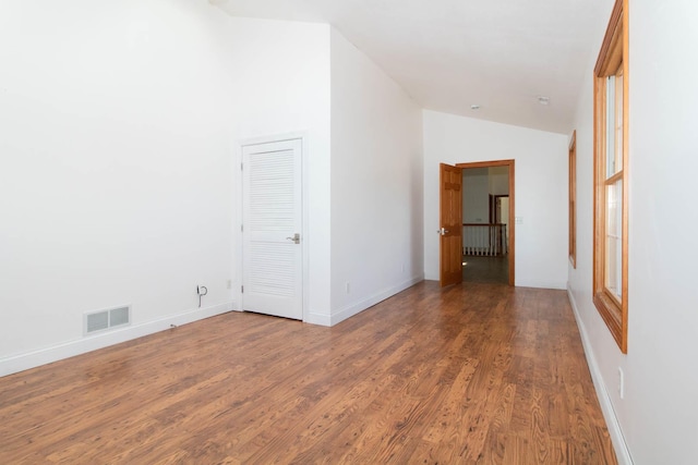 spare room with vaulted ceiling, visible vents, baseboards, and wood finished floors