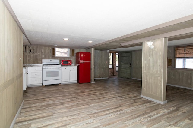kitchen with light wood-style floors, white gas range oven, wood walls, white cabinetry, and freestanding refrigerator