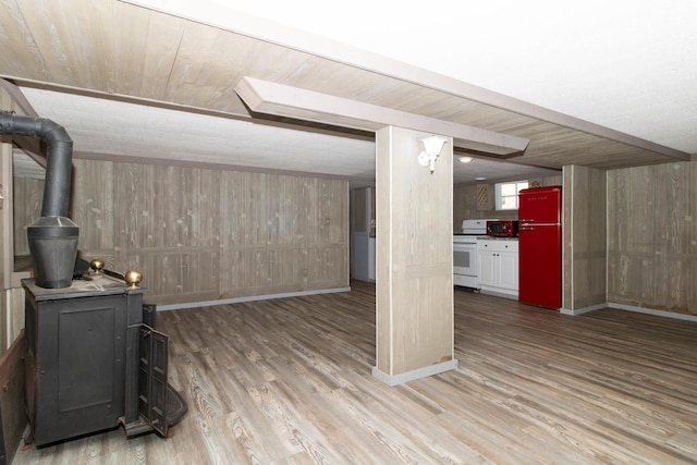 below grade area featuring wooden walls, a wood stove, baseboards, refrigerator, and light wood-style flooring