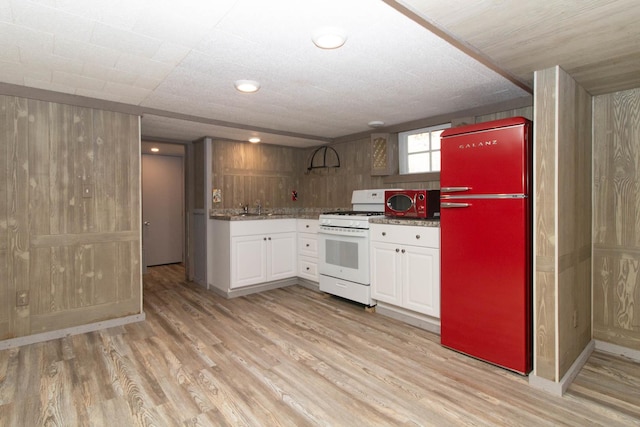 kitchen featuring white gas range, a sink, light wood finished floors, white cabinetry, and freestanding refrigerator