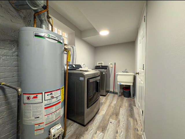 clothes washing area featuring laundry area, light wood-style floors, gas water heater, a sink, and washer and dryer