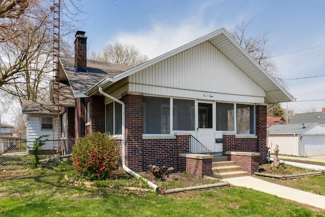 bungalow-style home with a sunroom, fence, a front lawn, brick siding, and a chimney