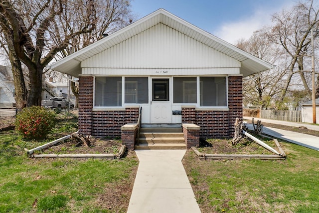 bungalow featuring brick siding, entry steps, a sunroom, and a front lawn
