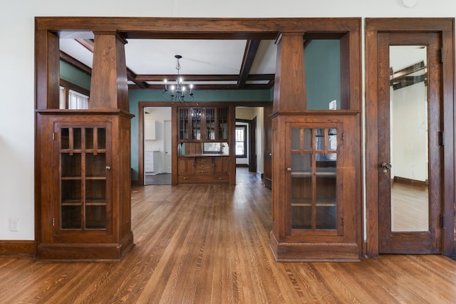 interior space featuring baseboards, a chandelier, beamed ceiling, coffered ceiling, and wood finished floors